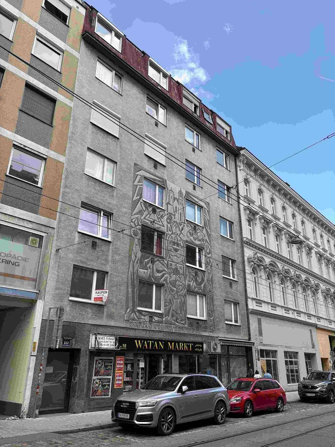 Mehrstöckiges Gebäude mit einer markanten Fassadenmalerei und Geschäften im Erdgeschoss.
