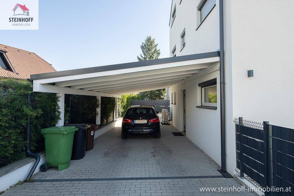 Überdachter Carport neben dem Haus mit gepflasterter Einfahrt und Platz für ein Fahrzeug.