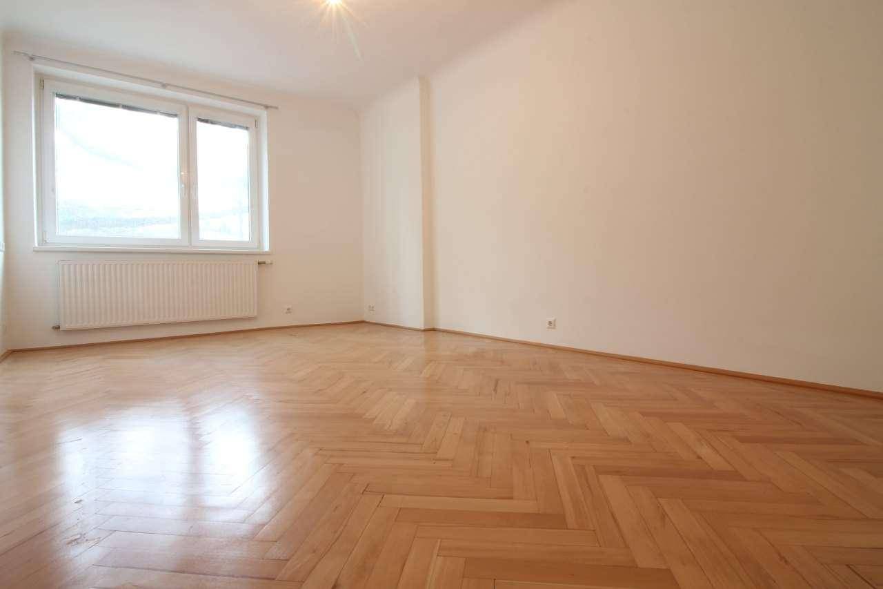 Geräumiges Zimmer mit Fischgrätparkett und großem Fenster, das für eine helle Atmosphäre sorgt.