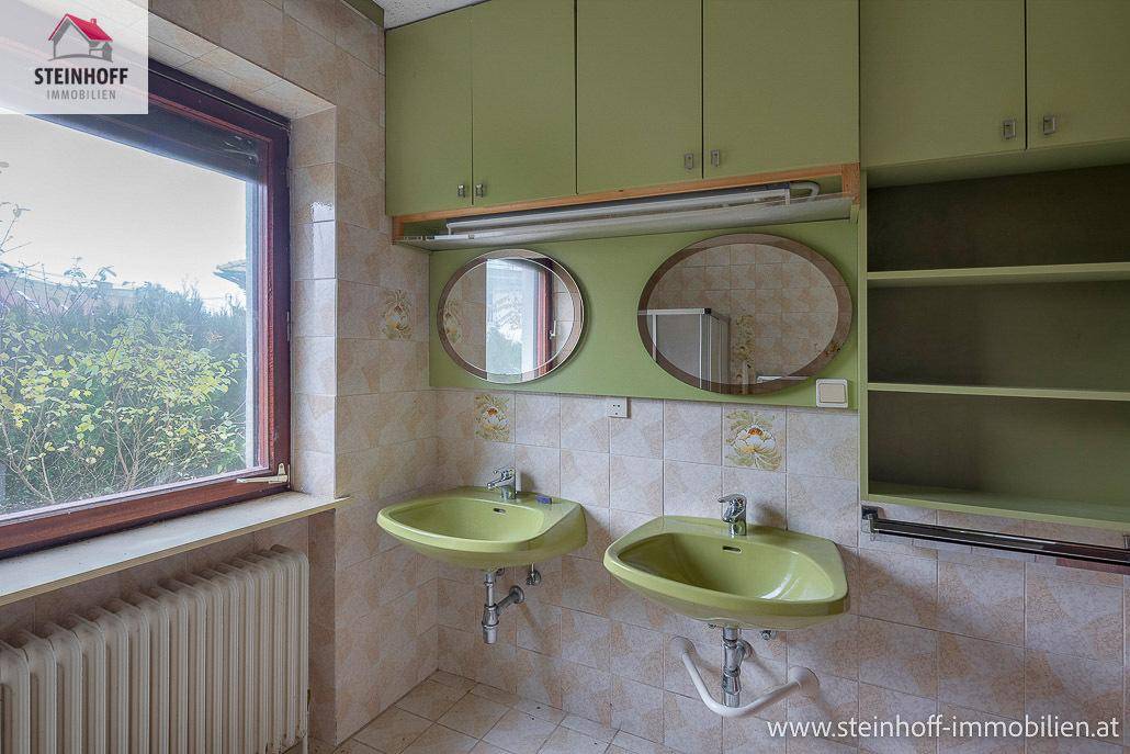 Badezimmer mit zwei grünen Waschbecken, Spiegelschränken und Fenster.