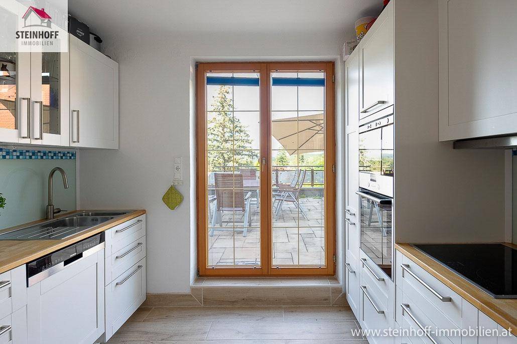 Helle Einbauküche mit weißen Schränken, Holztheke und Blick auf die Terrasse.