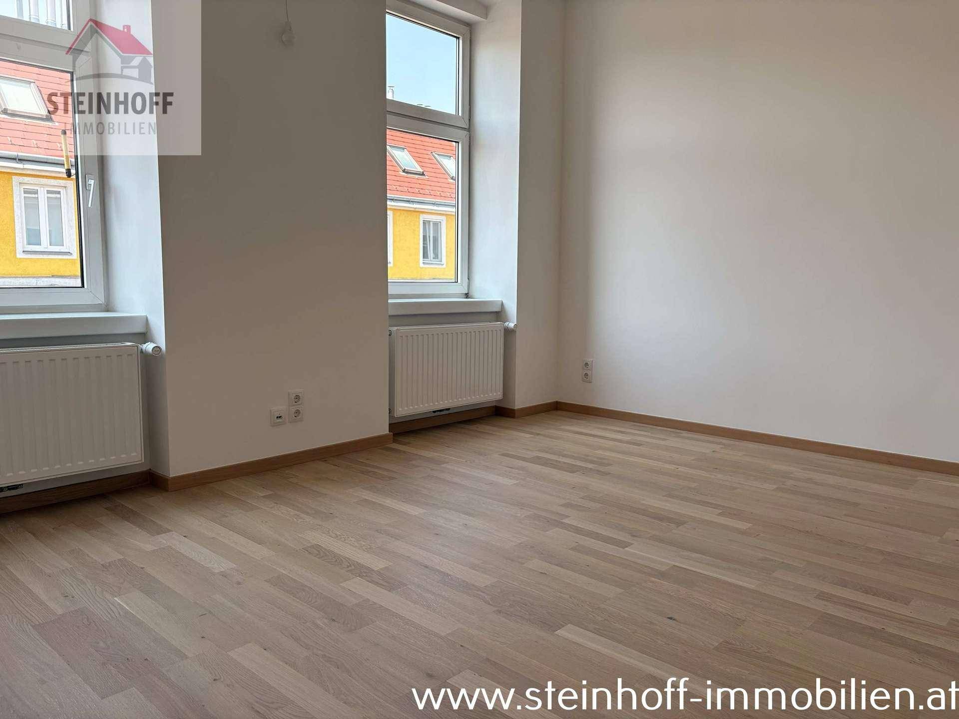Geräumiges Zimmer mit Parkettboden und zwei Fenstern, die viel natürliches Licht hereinlassen.