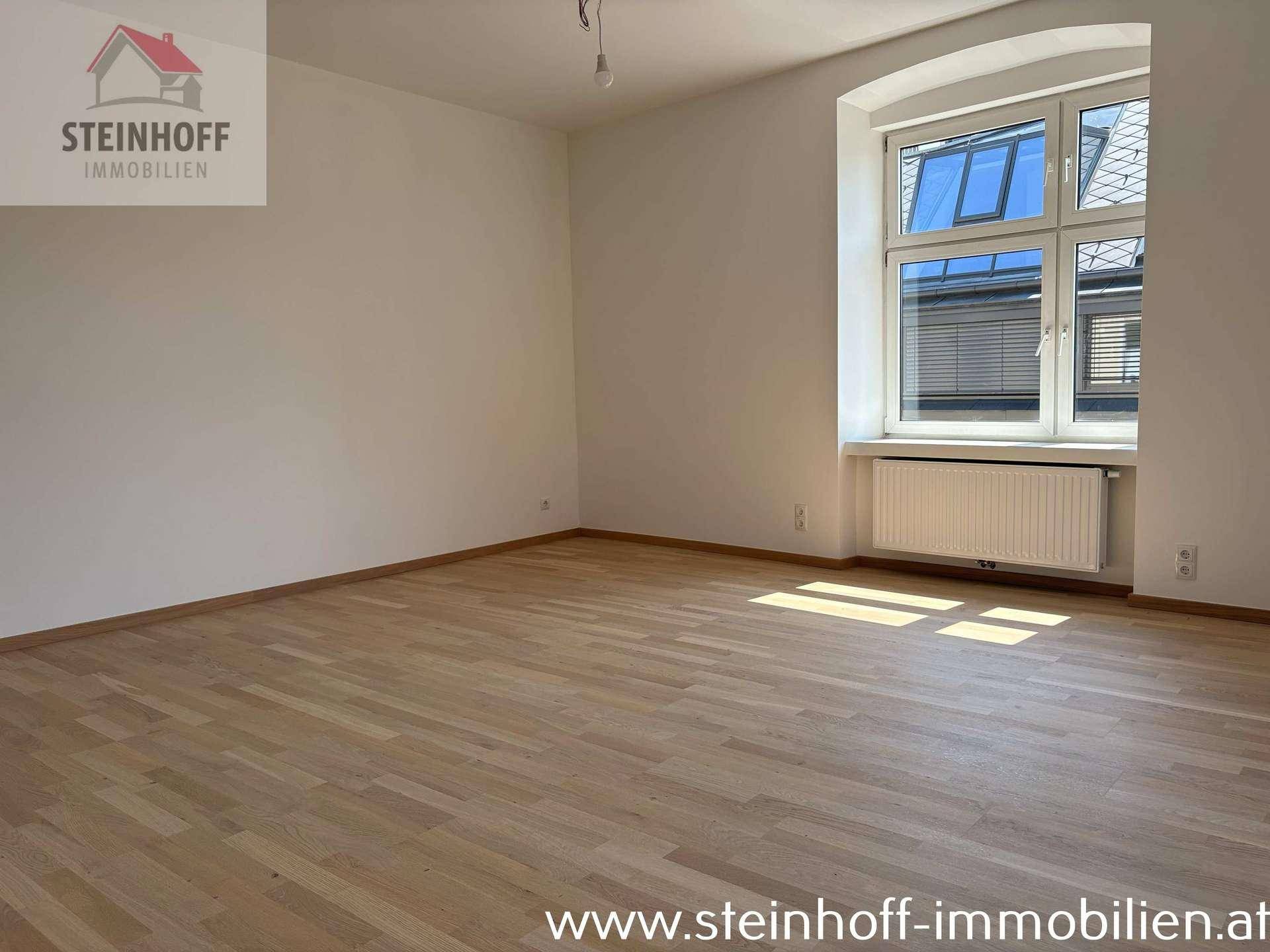 Leeres Zimmer mit Parkettboden und einem großen Fenster, das den Raum mit natürlichem Licht füllt.