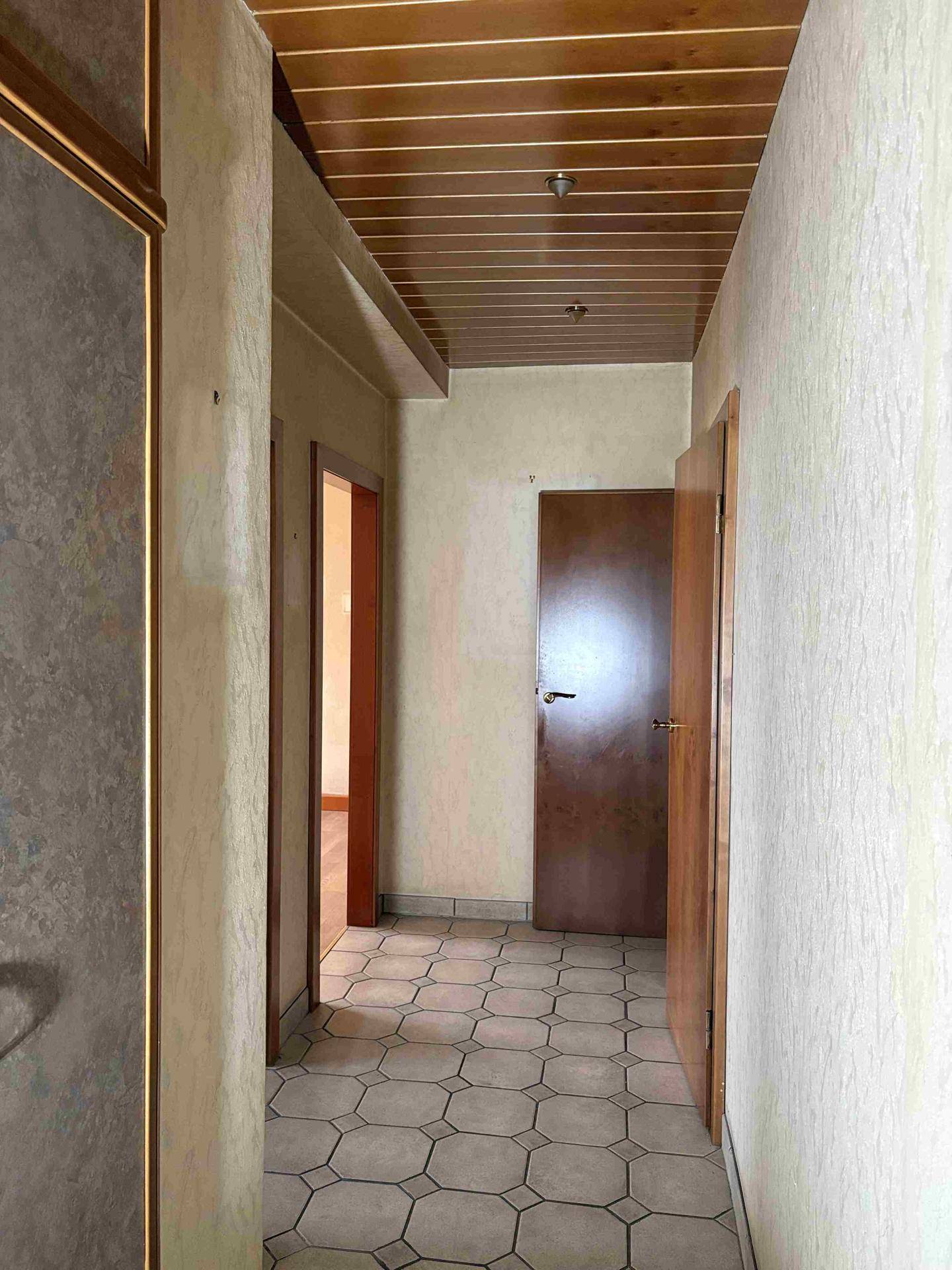 Langer Flur mit Fliesenboden und Holzdecke, der zu verschiedenen Zimmern führt.