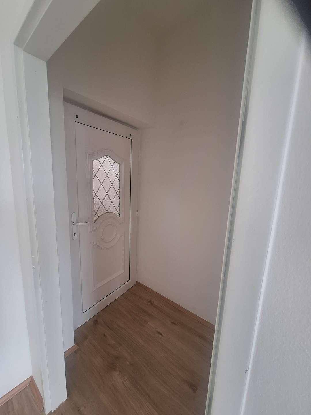 Eingangsbereich mit hellem Laminatboden und einer weißen Eingangstür mit dekorativem Glaseinsatz, wirkt einladend.