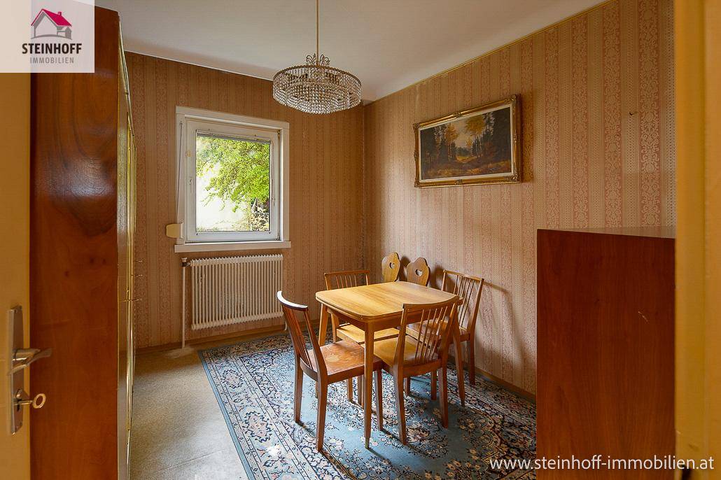 Kleiner Essbereich mit Holztisch, Stühlen und einem Teppich, beleuchtet durch ein Fenster.