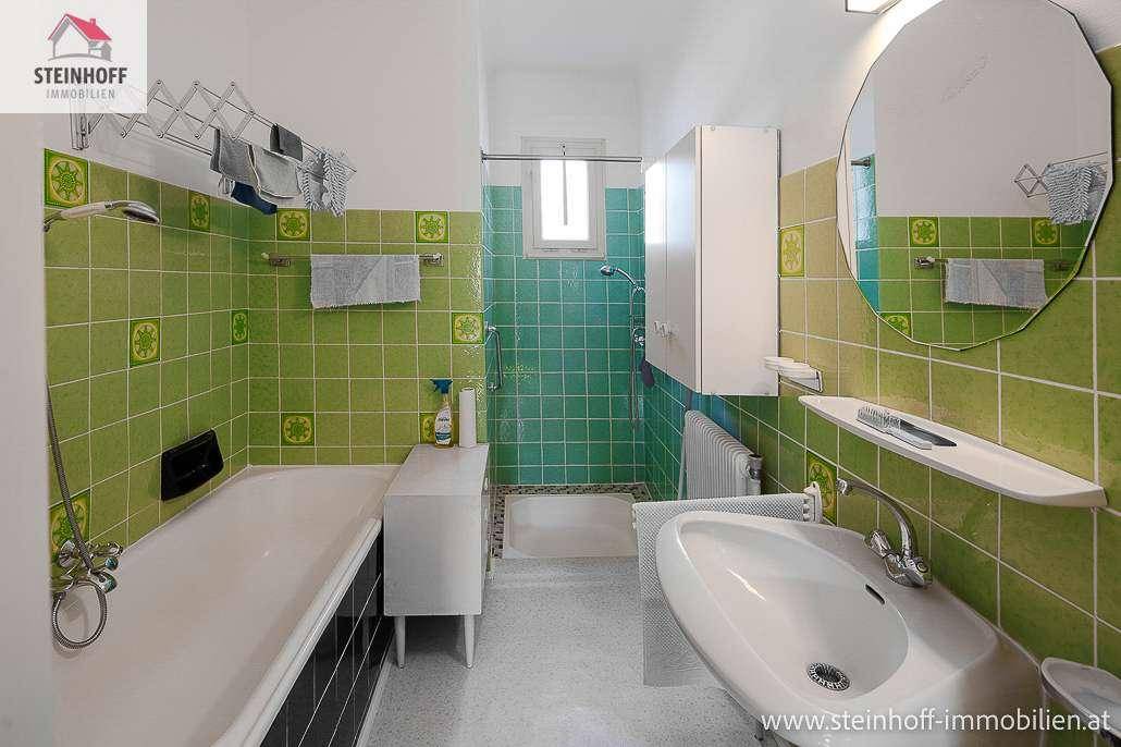 Badezimmer mit grünen und weißen Fliesen, Badewanne, Dusche und Waschbecken.