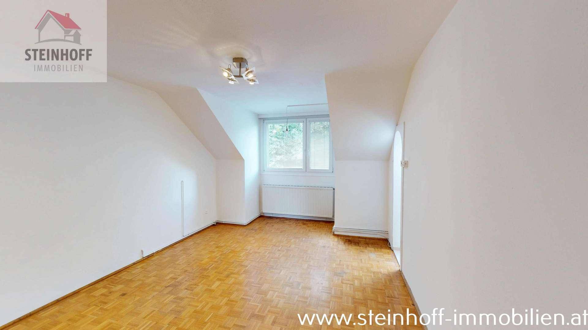 Helles Schlafzimmer mit Parkettboden, Fenster und charakteristischen Dachschrägen.