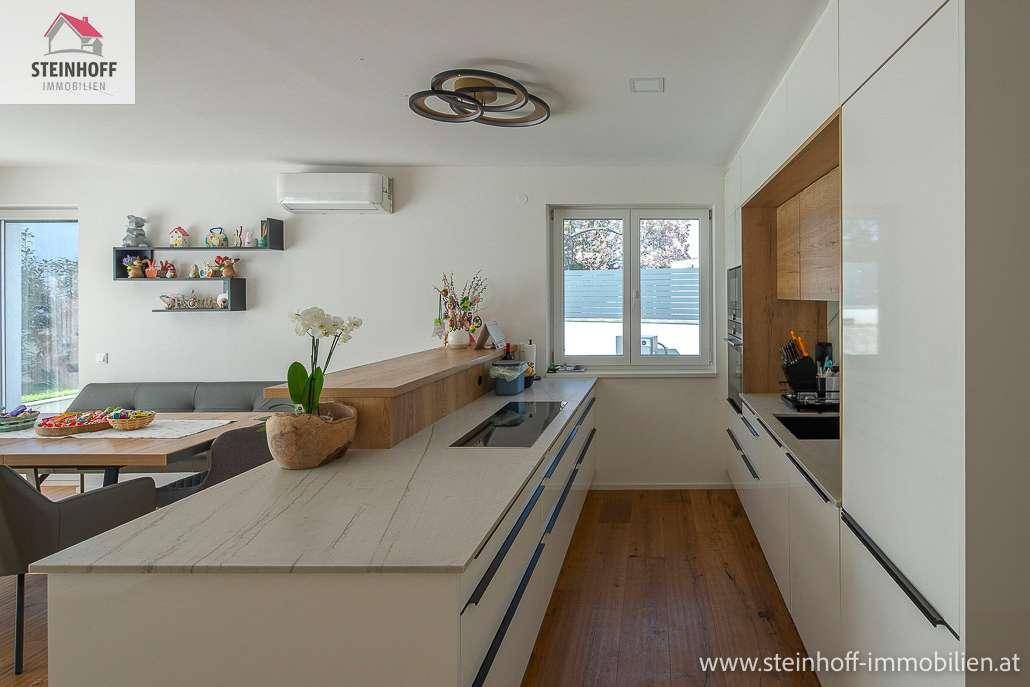 Moderne weiße Einbauküche mit Holztheke, Induktionskochfeld und integriertem Backofen.