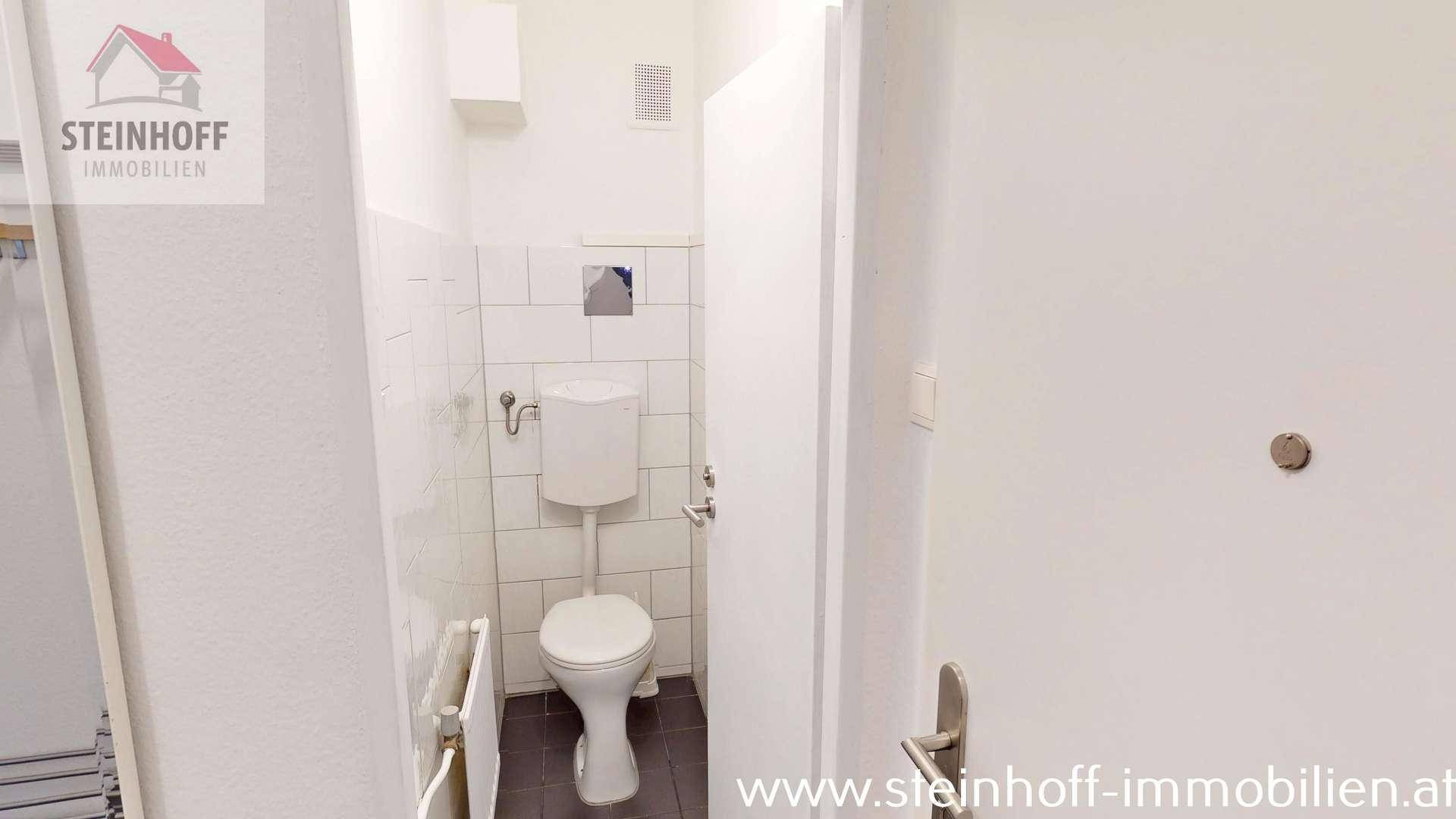 Separates WC mit Toilette und weißen Fliesen an den Wänden.