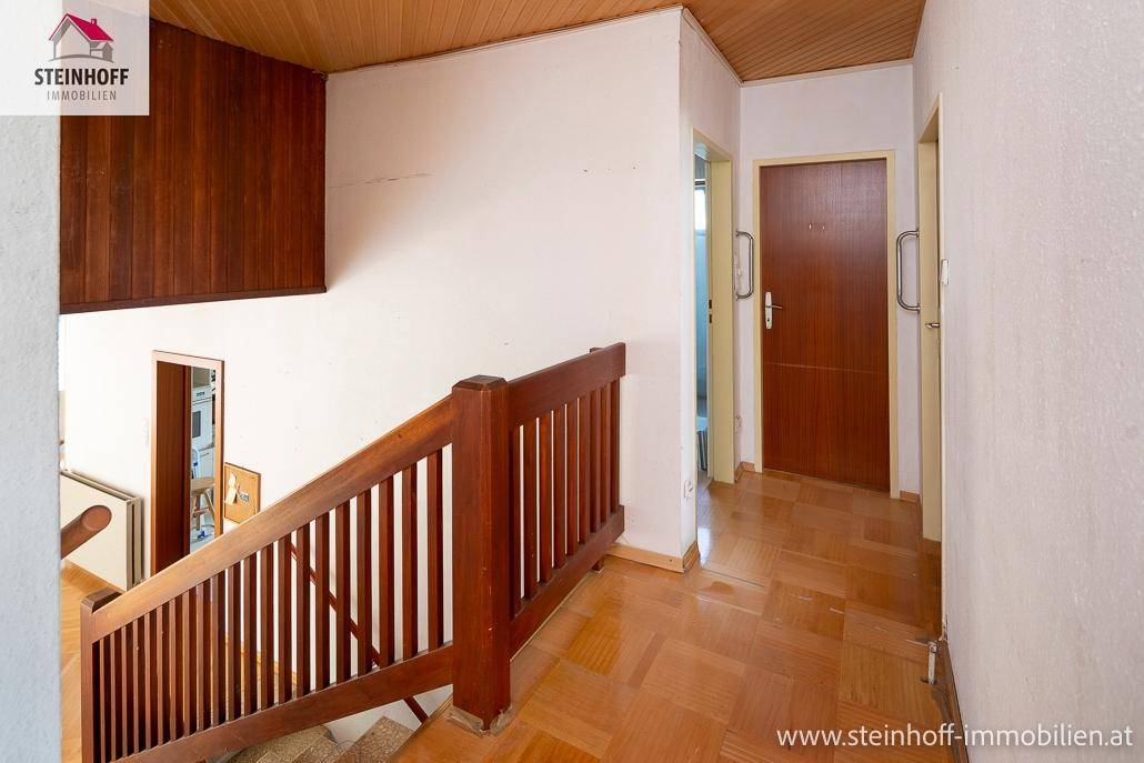Heller Flur mit Holzparkett, Holzdecke und einer Holztreppe, die zu den oberen Etagen führt.