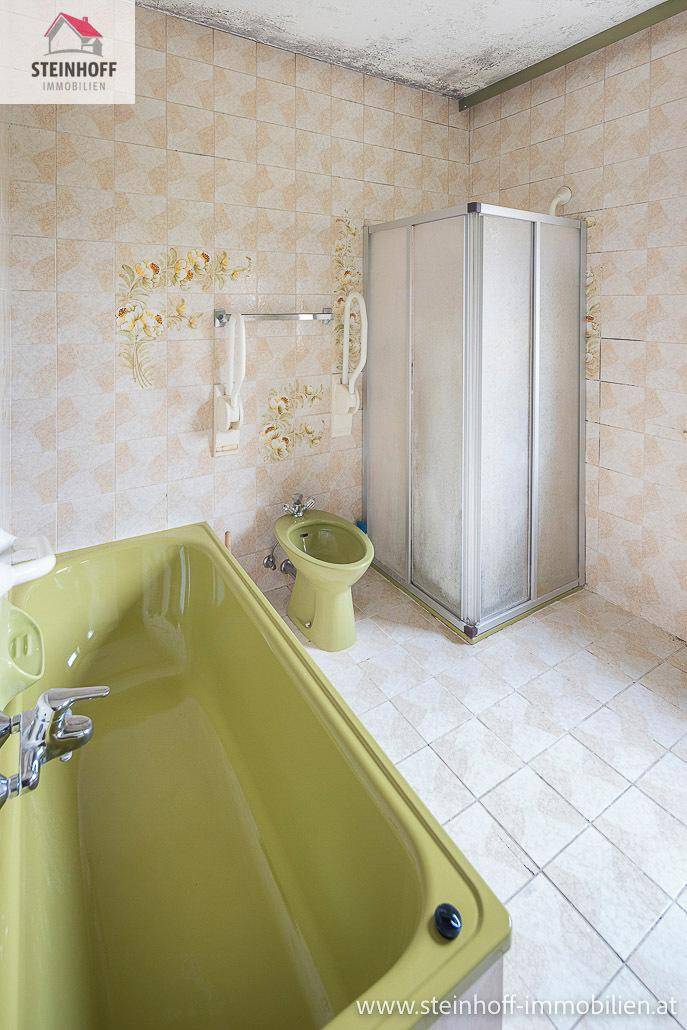 Badezimmer im Stil der 80er Jahre mit grüner Badewanne, Bidet und Duschkabine.