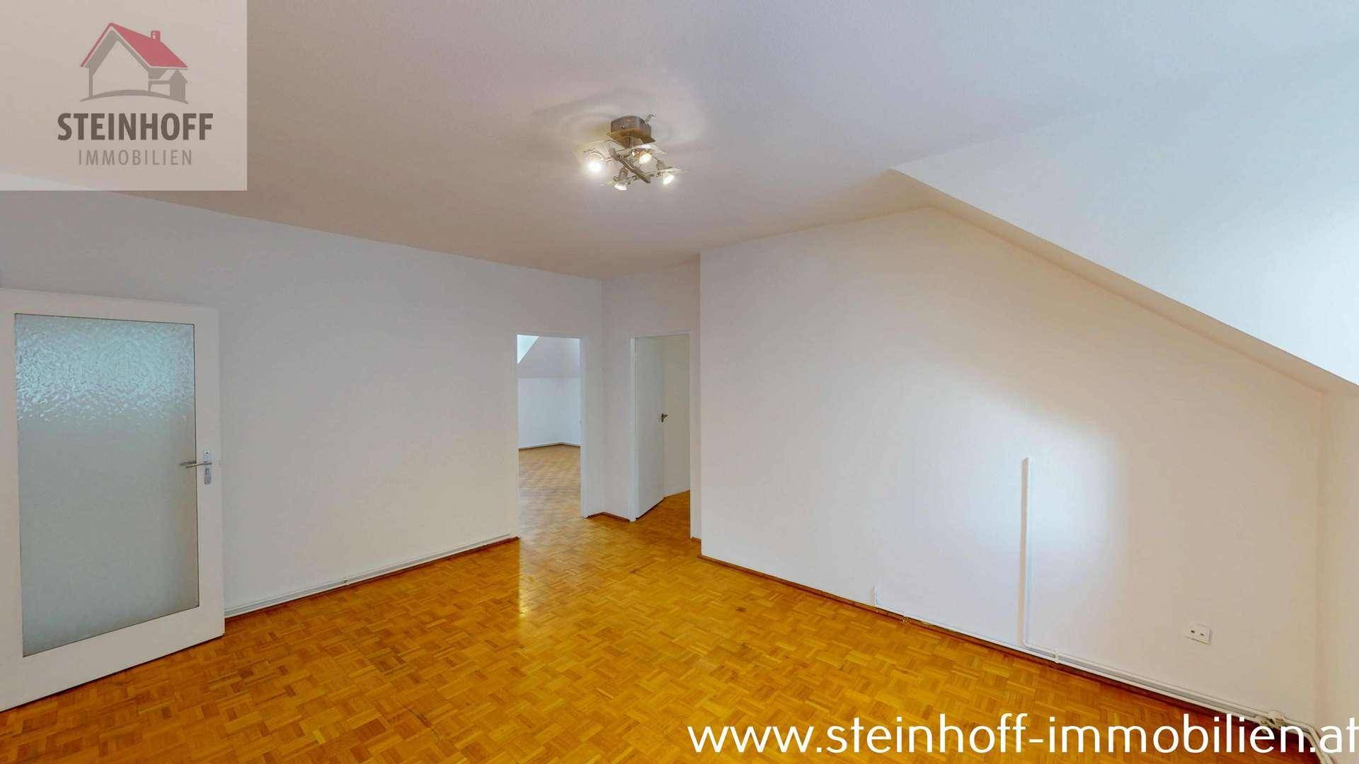 Geräumiger Raum mit Parkettboden, Dachschrägen und mehreren Türen.
