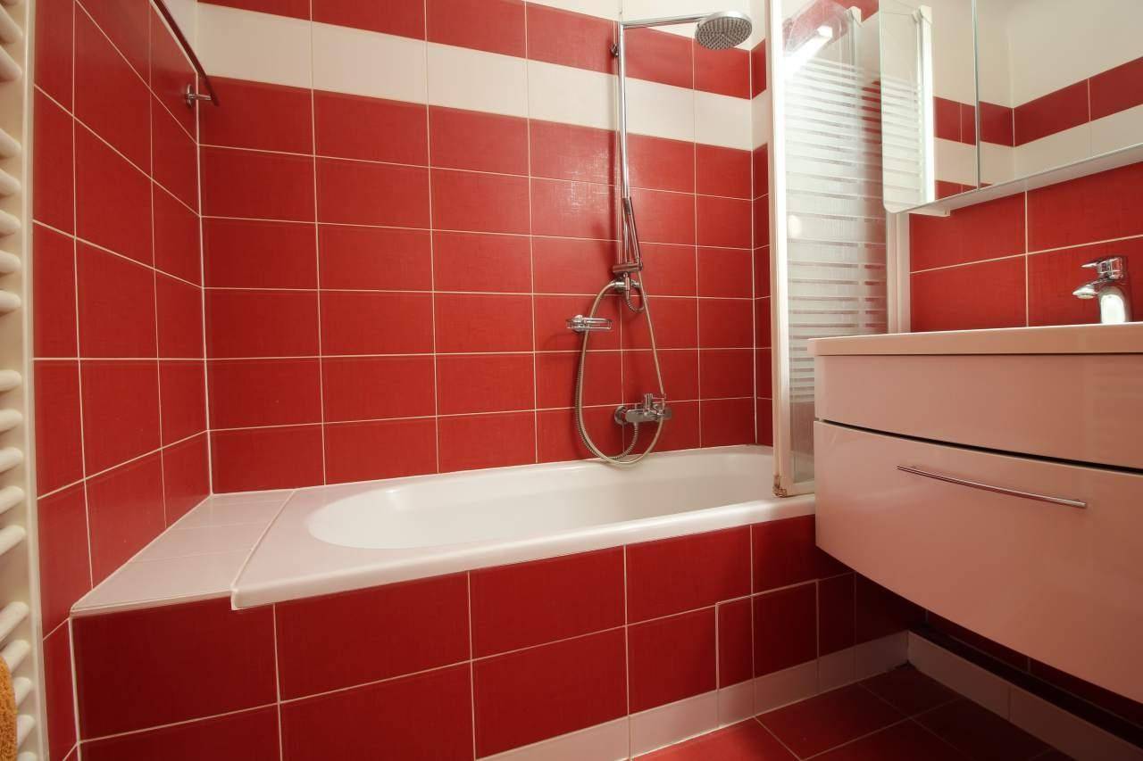 Helles Badezimmer mit roten und weißen Fliesen, Badewanne mit Duschvorrichtung und Spiegel.