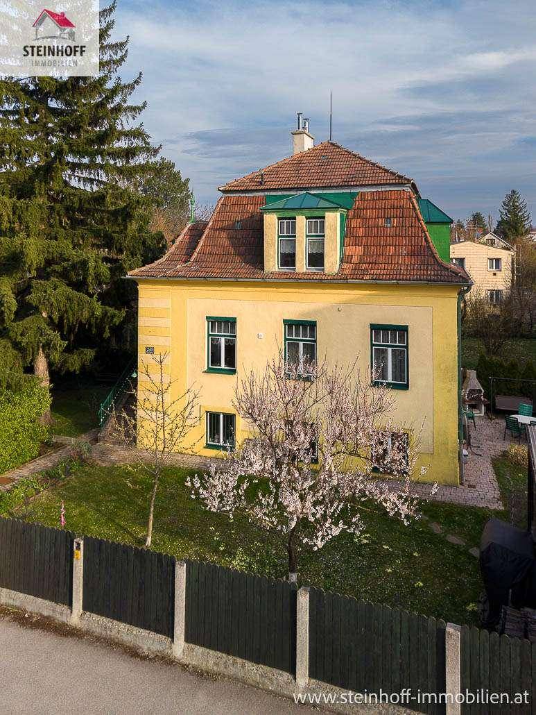 Historisches gelbes Gebäude mit Mansarddach und blühendem Baum im Vorgarten.
