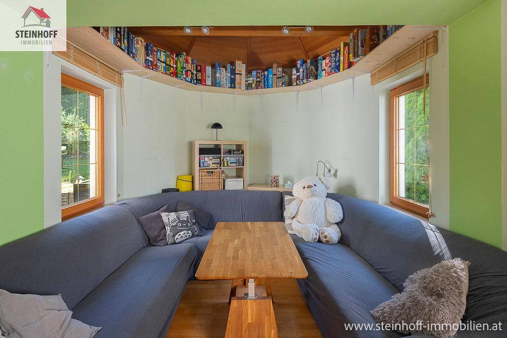 Gemütliche Sitzecke mit Bücherregal und Blick ins Grüne durch große Fenster.