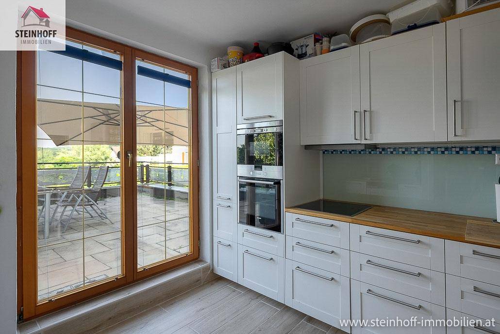 Moderne weiße Küche mit Einbaugeräten, Holzarbeitsplatte und Terrassenzugang.