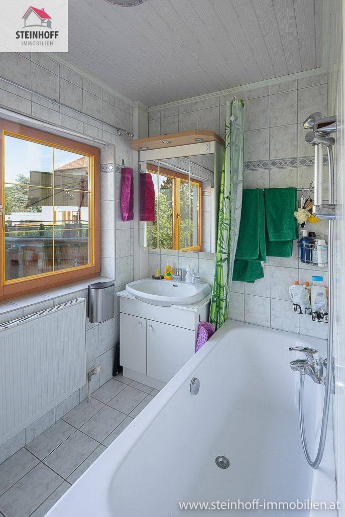 Helles Badezimmer mit Badewanne, Waschbecken, Fenster und weißen Fliesen.