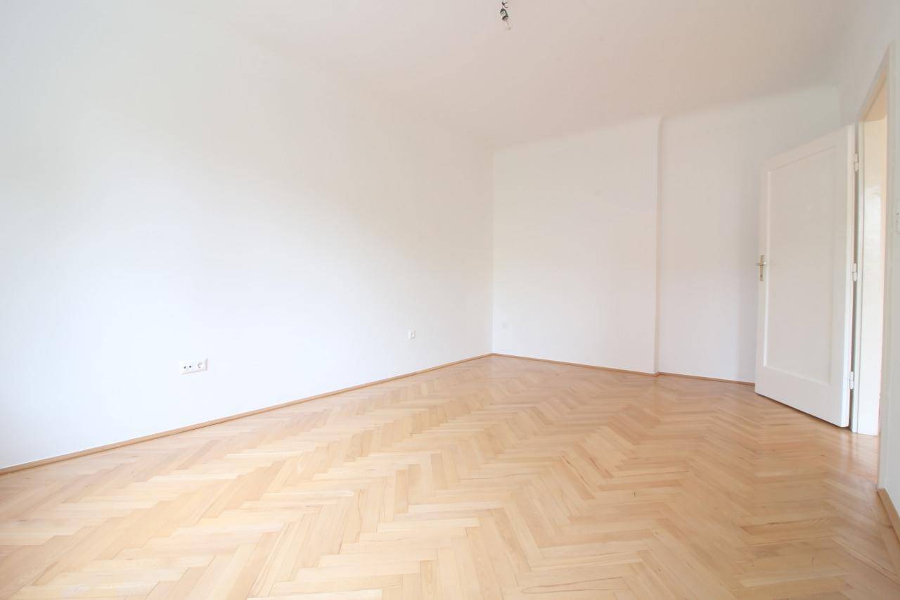 Leerer Raum mit hellem Fischgrätparkett und weißen Wänden, bereit zur individuellen Gestaltung.