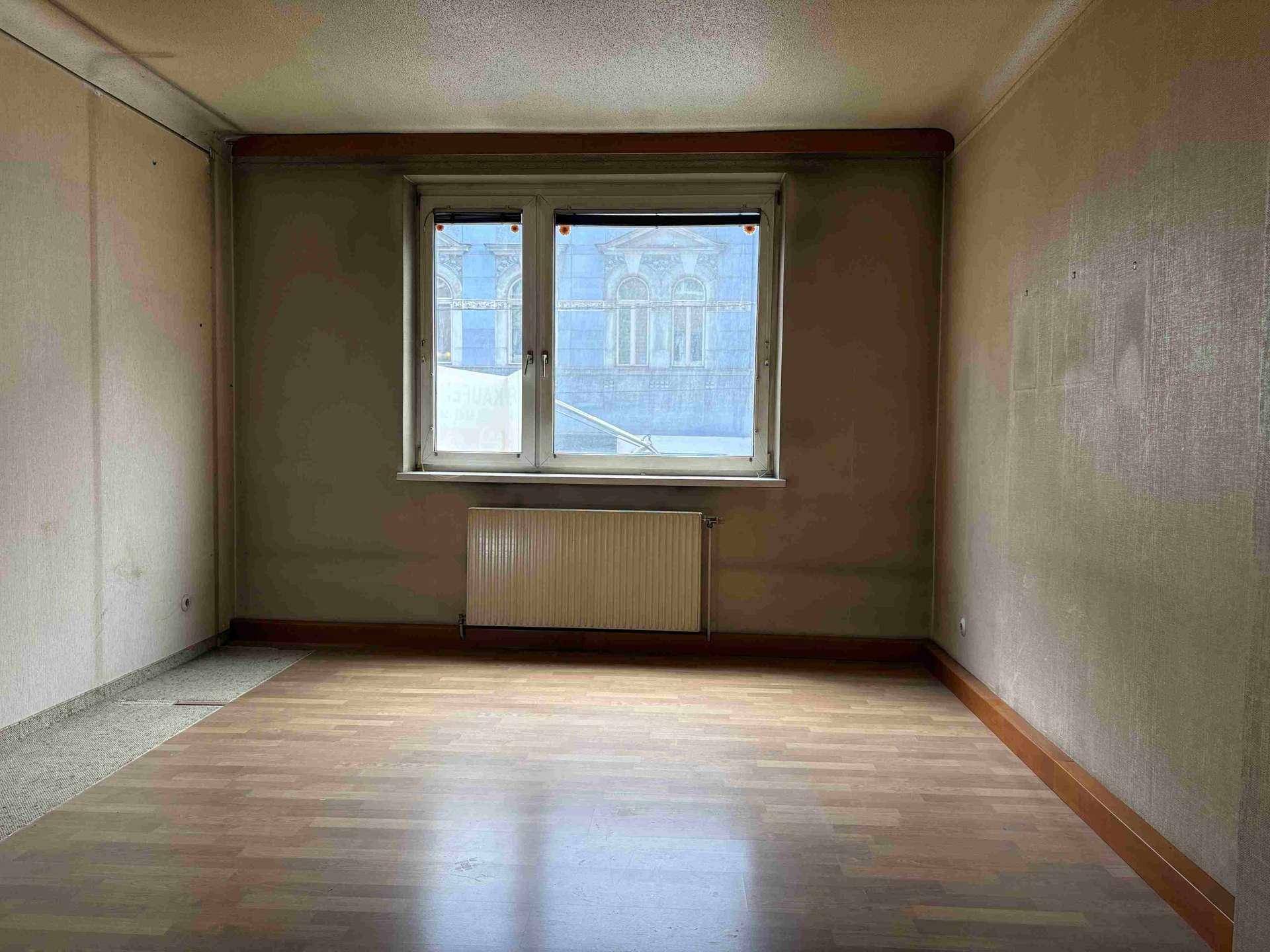 Leeres Zimmer mit Laminatboden, Heizkörper und Blick auf die gegenüberliegende Fassade.