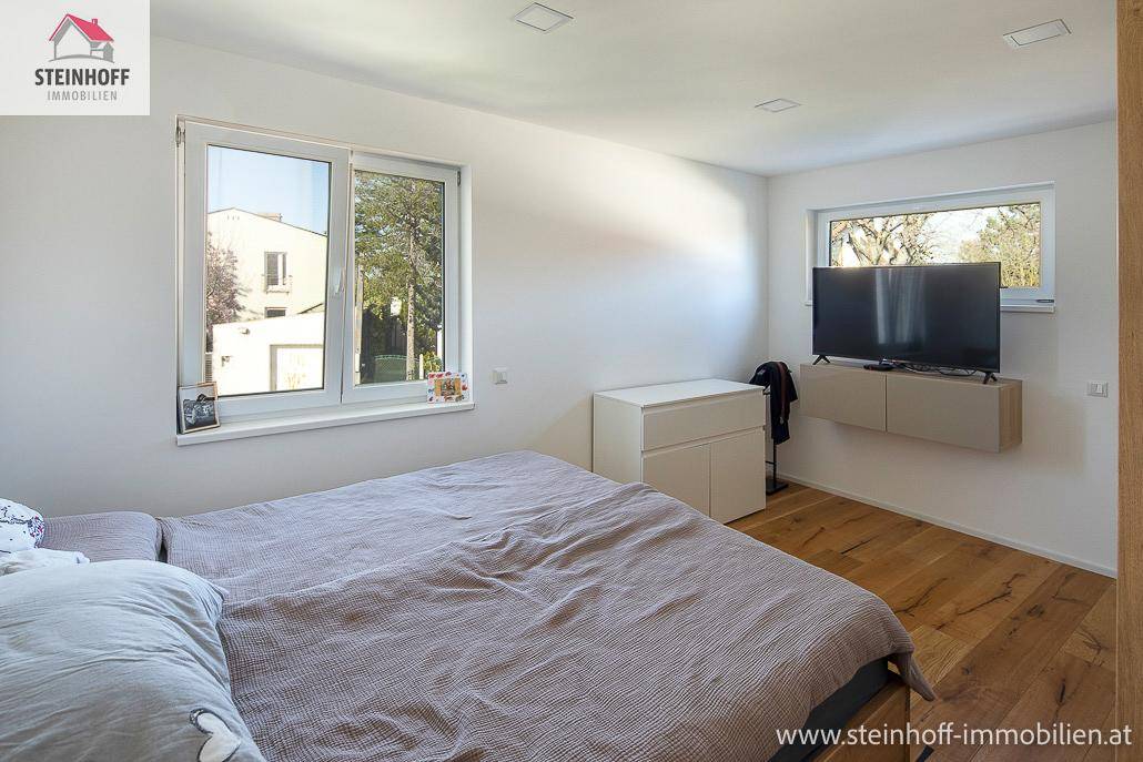 Helles Schlafzimmer mit Holzboden, großen Fenstern und moderner, minimalistischer Einrichtung.