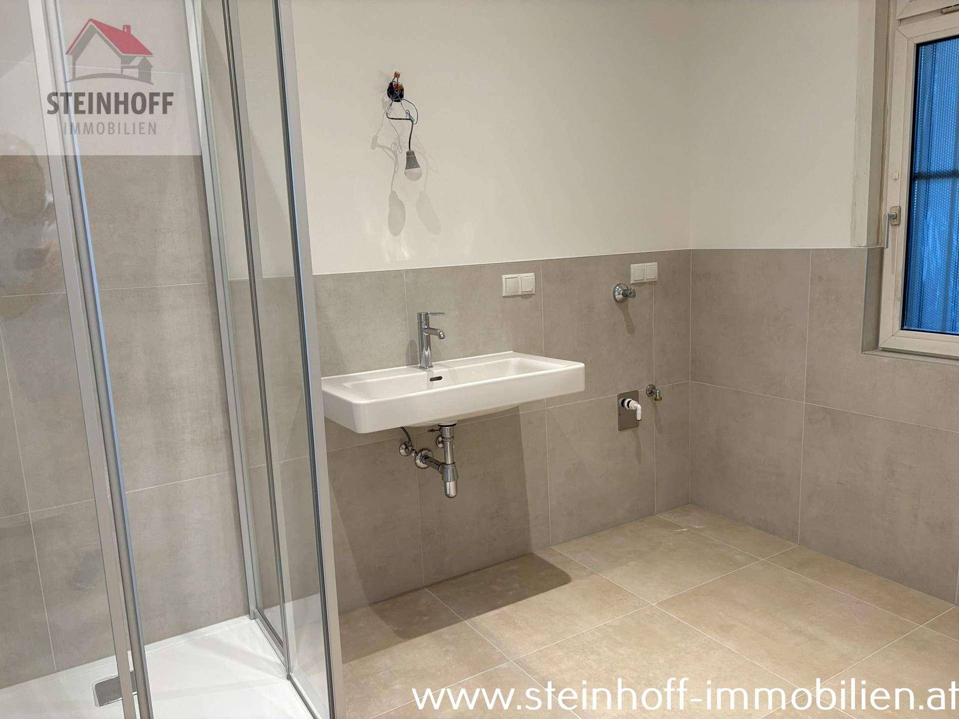 Helles Badezimmer mit modernem Waschbecken, Duschkabine und hellgrauen Fliesen.