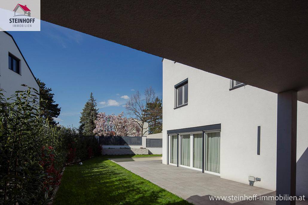 Gepflegter Gartenbereich mit Rasenfläche und gepflasterter Terrasse neben dem Haus, ideal zum Verweilen.