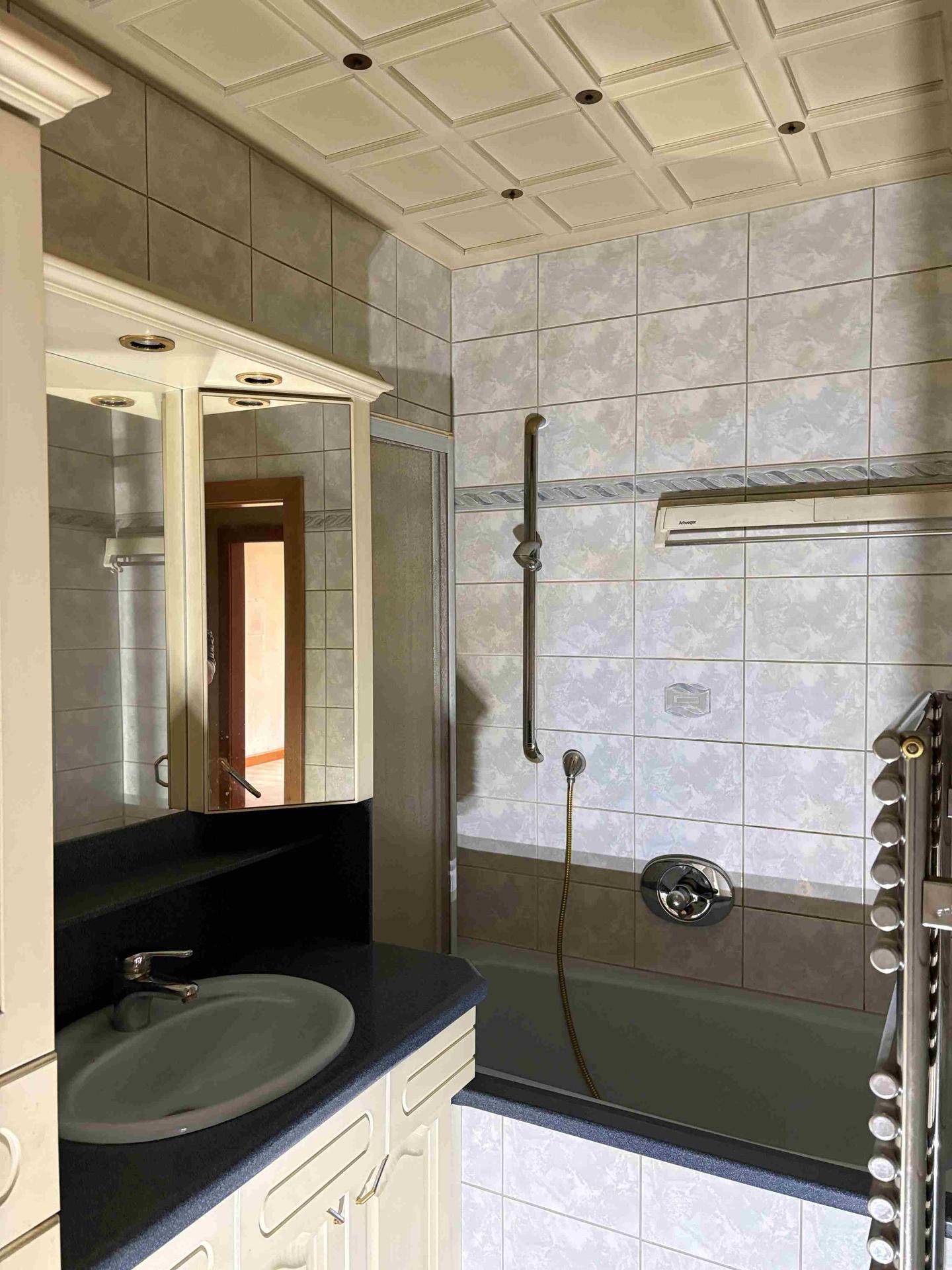 Badezimmer mit Badewanne, Waschbecken und Spiegelschrank, gefliest in hellen Tönen.