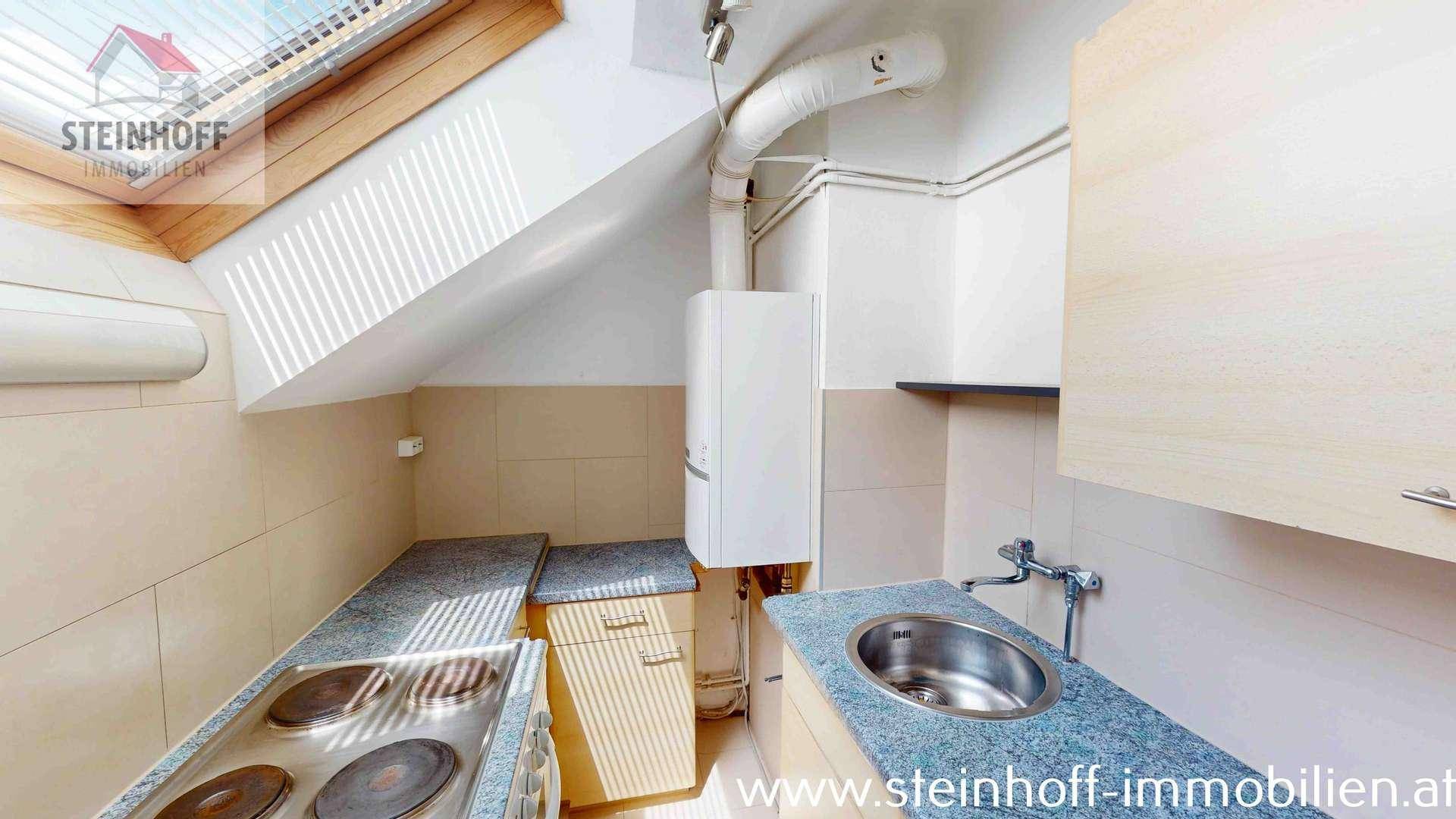 Kleine Küche mit Dachfenster, Kochfeld, Spüle und Dachschrägen.