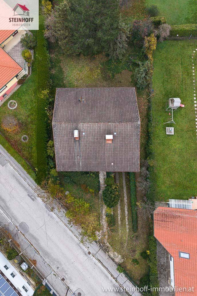 Luftaufnahme eines Einfamilienhauses mit Garten und angrenzender Straße.
