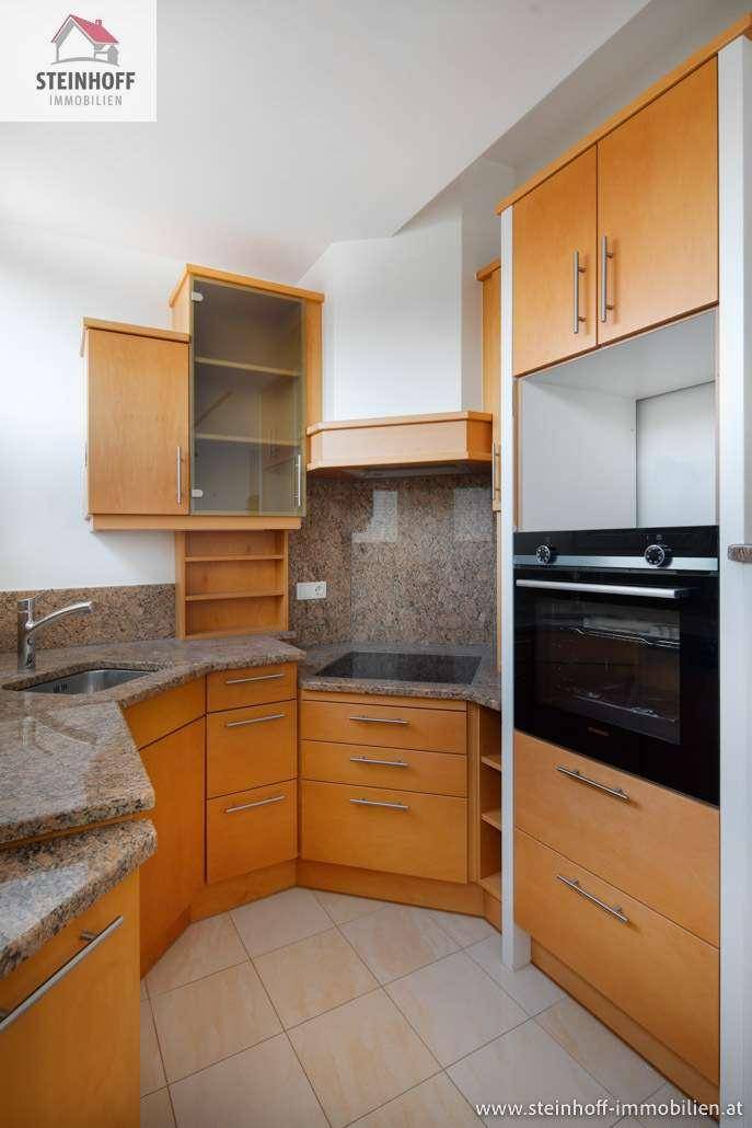 Moderne Küche mit Holzschränken, Granitarbeitsplatten und integriertem Backofen und Kochfeld.