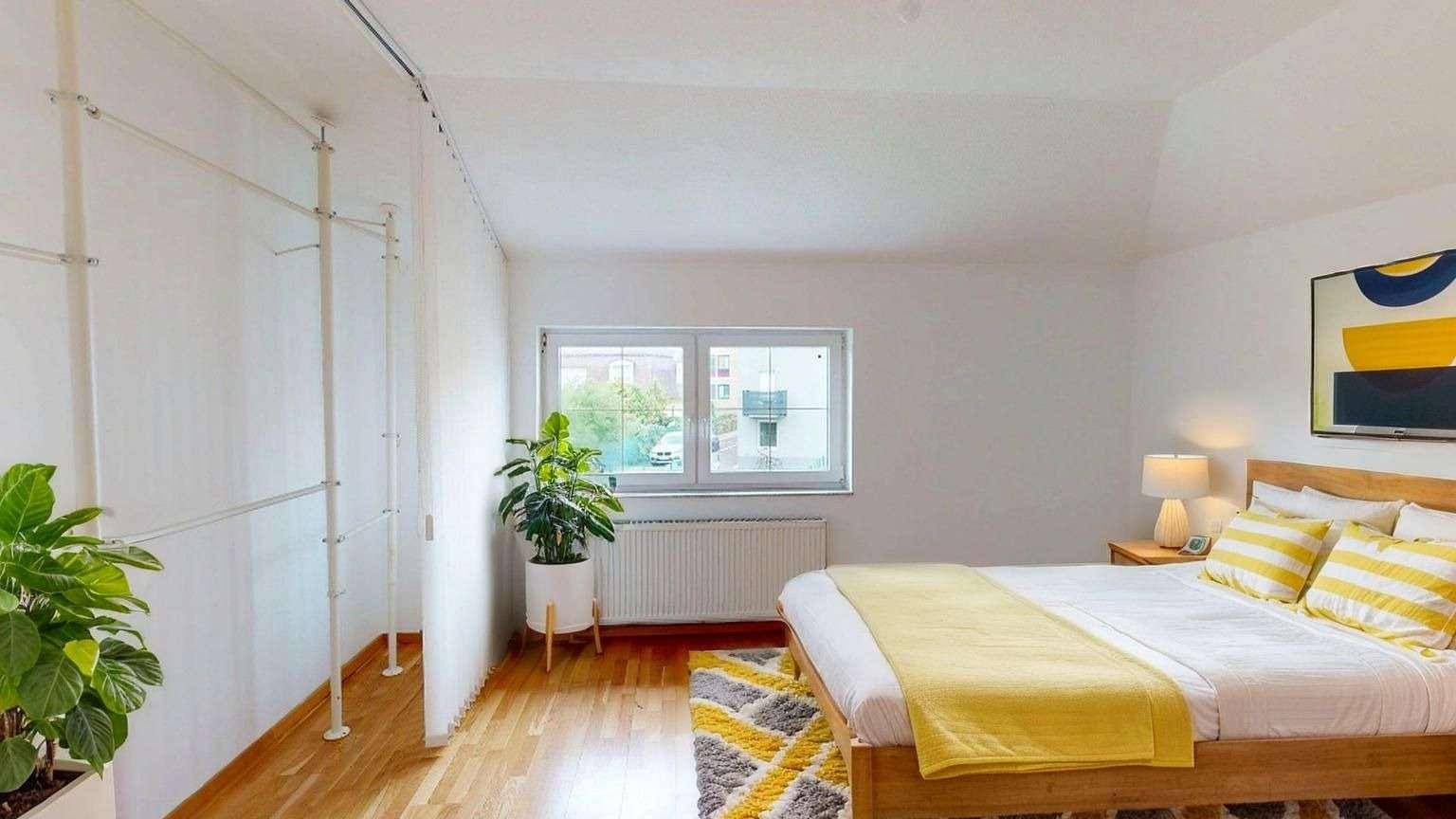 Helles Schlafzimmer mit Holzboden, großem Bett und offener Kleideraufbewahrung, modern eingerichtet.