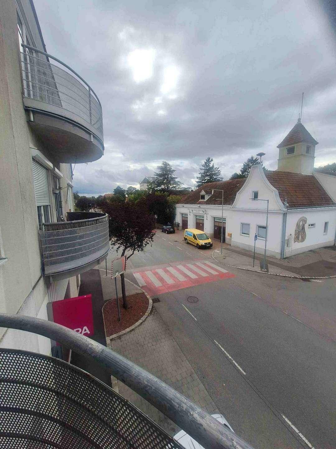 Blick vom Balkon auf eine Straßenkreuzung mit Zebrastreifen und ein charmantes älteres Gebäude mit markantem Dach.