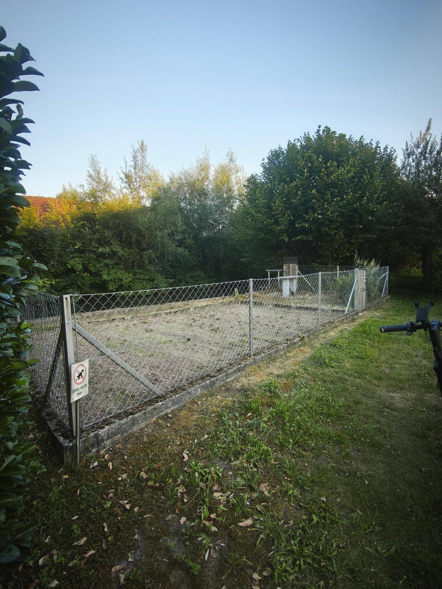 Eingezäunter Gartenbereich mit einem kleinen Steintisch und üppiger Vegetation.
