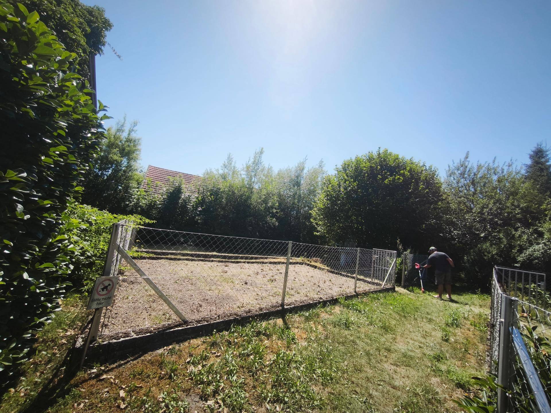 Sonniges Gartengrundstück mit Zaun und einer Person, die im Hintergrund arbeitet.