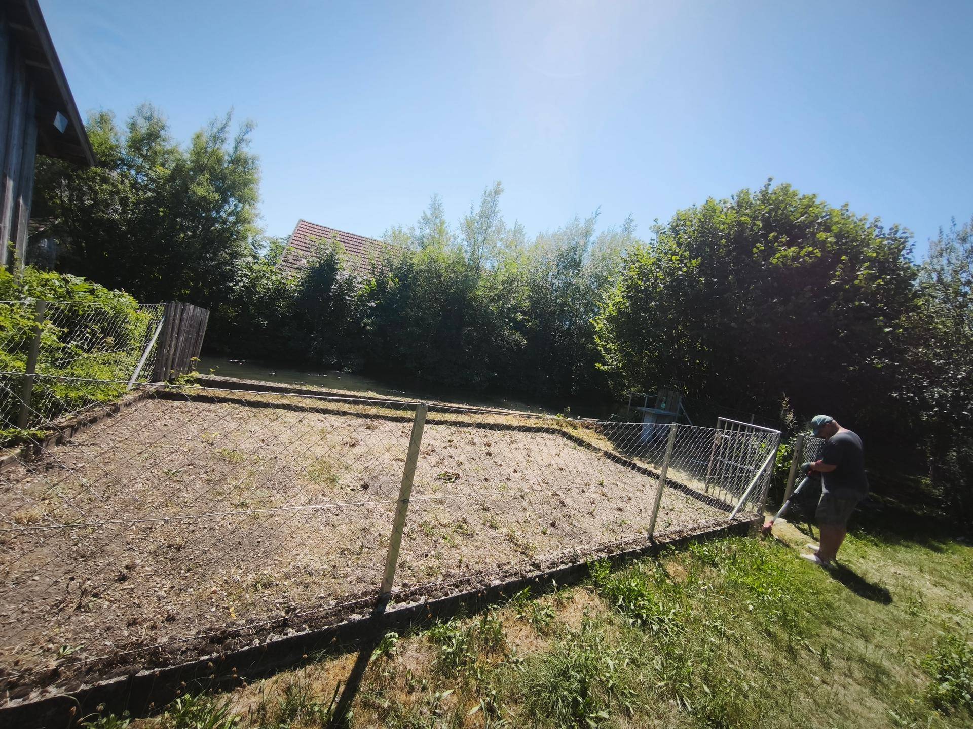 Sonniges Gartengrundstück mit Zaun und einer Person, die im Hintergrund arbeitet.