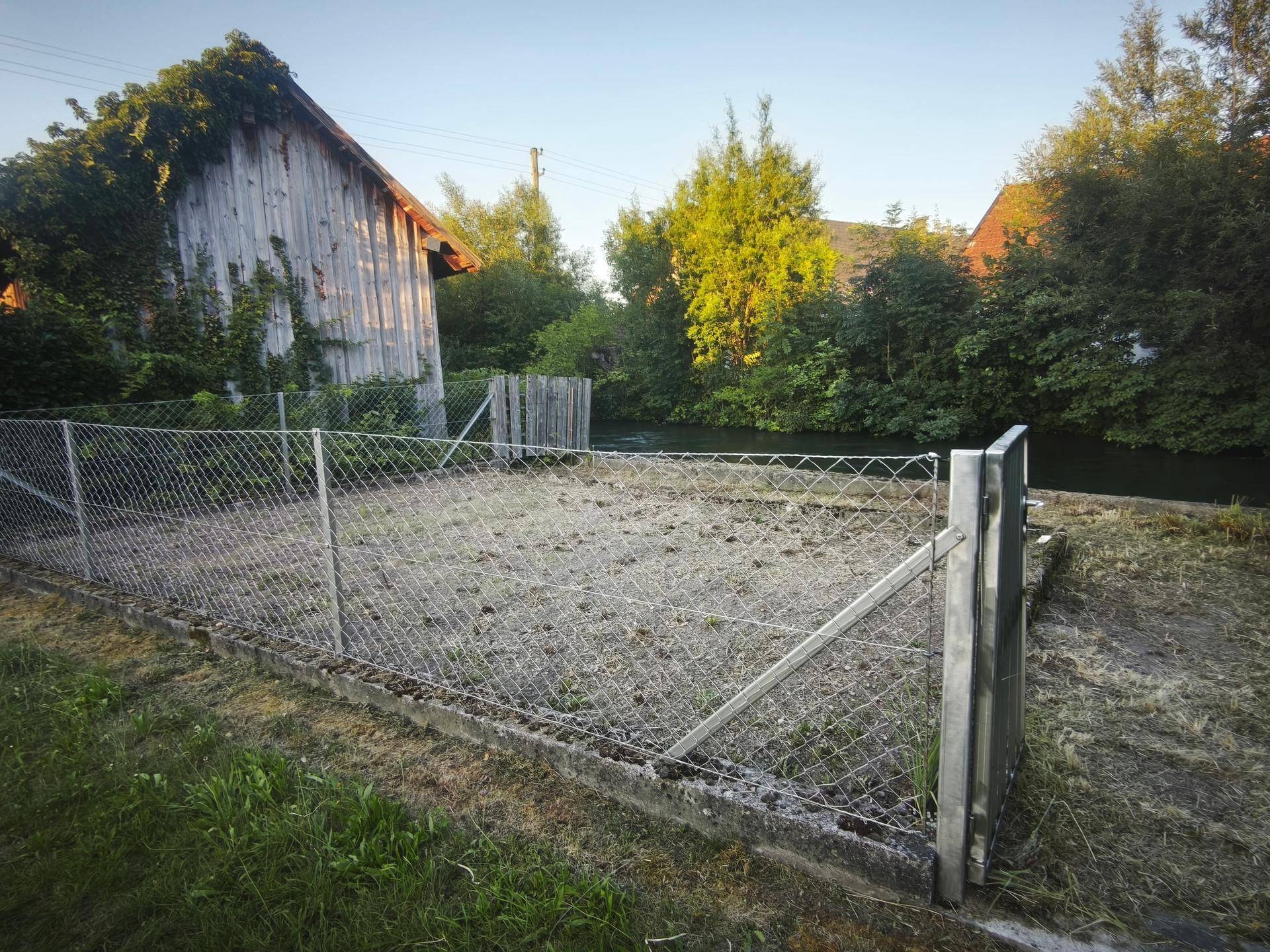 Eingezäunter Gartenbereich mit Blick auf den Fluss und einen alten Holzschuppen.