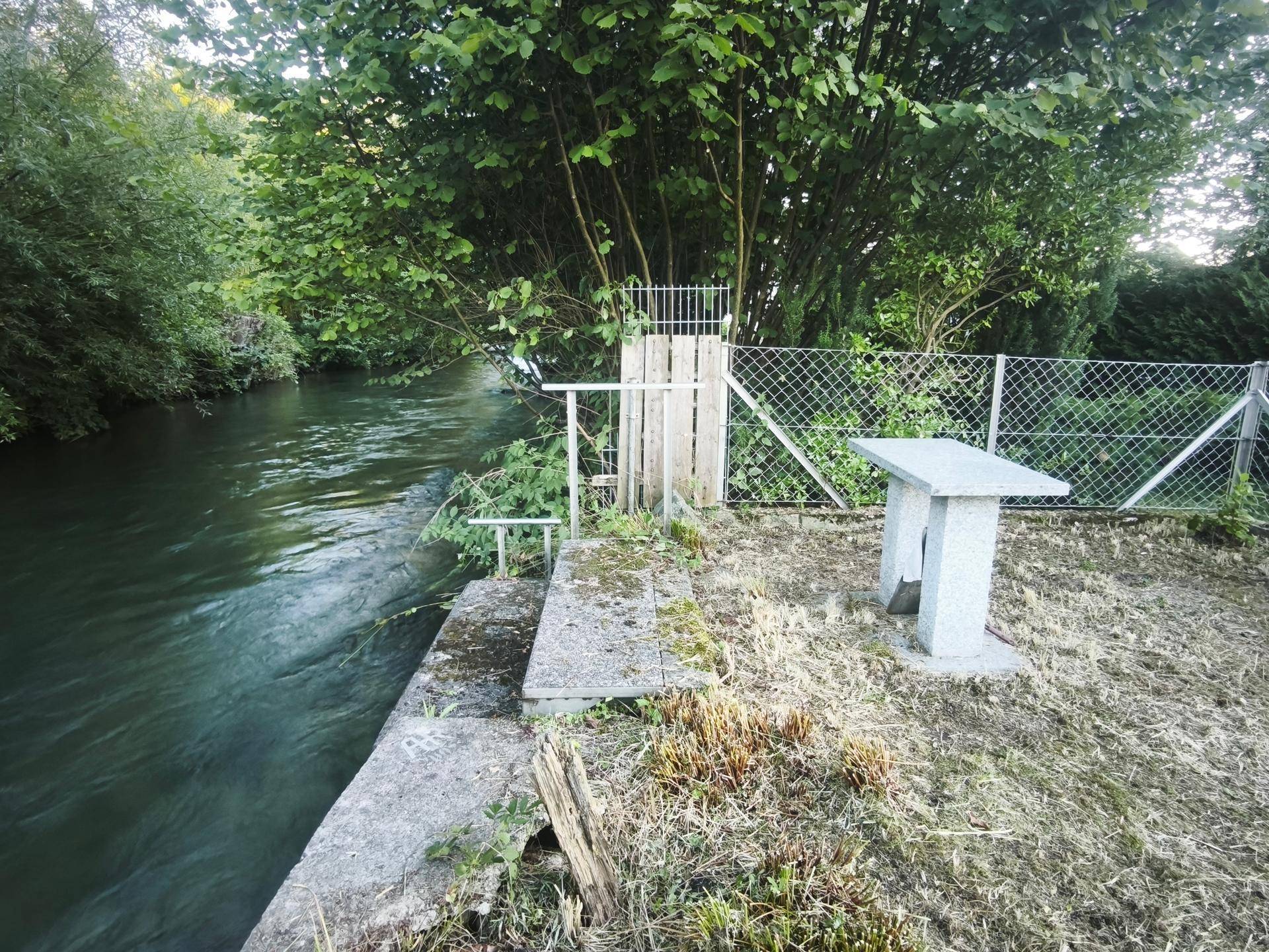 Steintisch am Flussufer mit Blick auf die dichte Vegetation und das fließende Wasser.