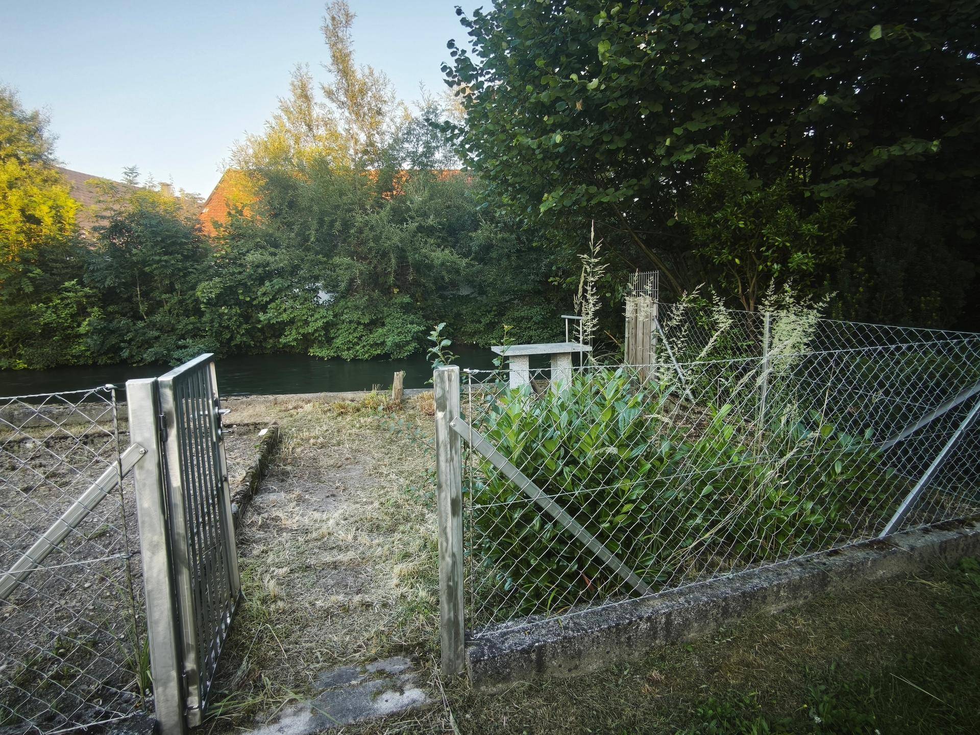 Blick durch das Gartentor auf den Fluss und die umliegende dichte Vegetation.