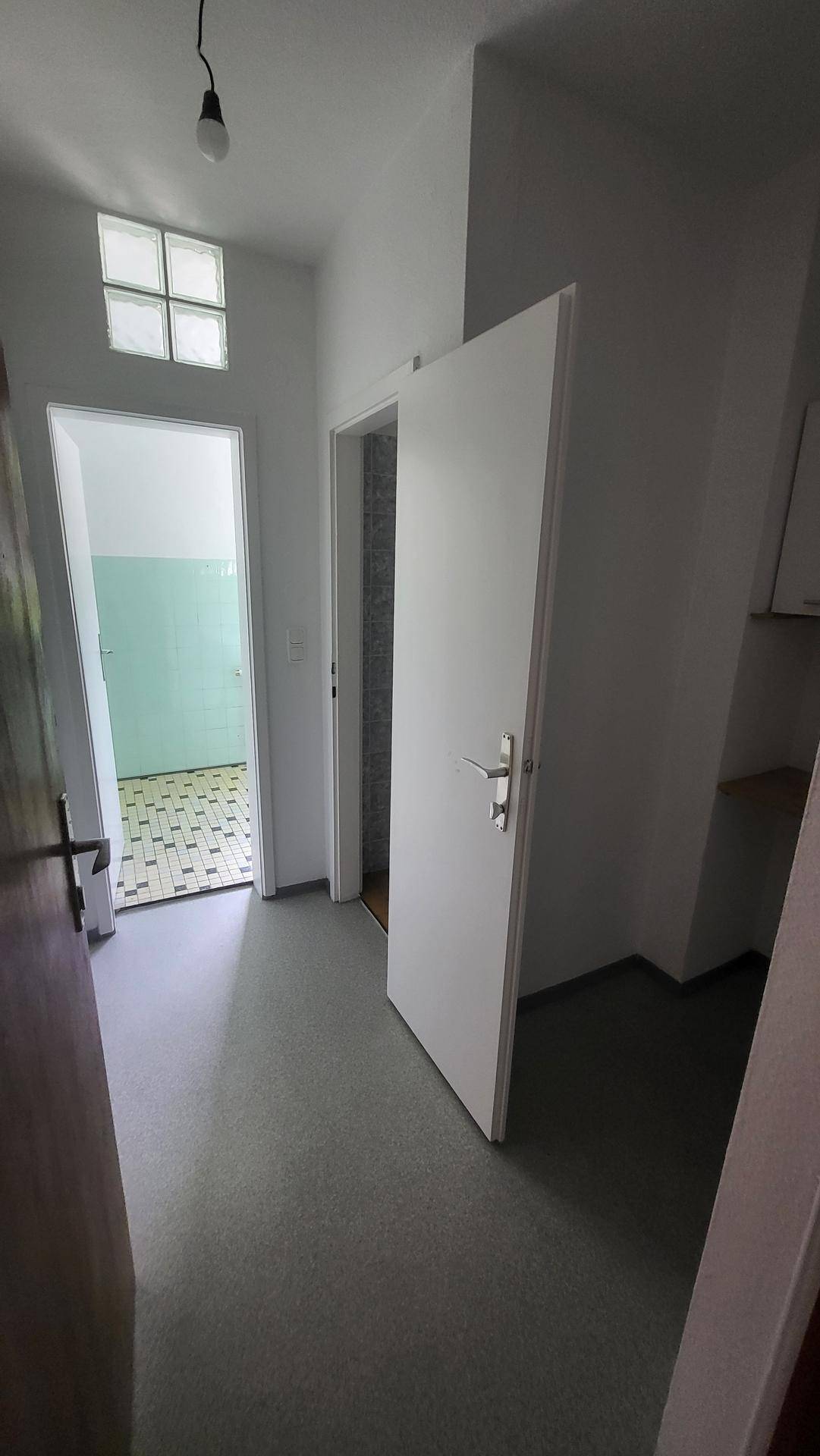 Heller Flur mit mehreren Türen und einem kleinen Oberlichtfenster, das Tageslicht hereinlässt.