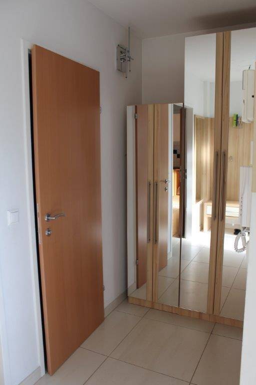 Flur mit hellem Fliesenboden, einer Holztür und einem großen Spiegelschrank.
