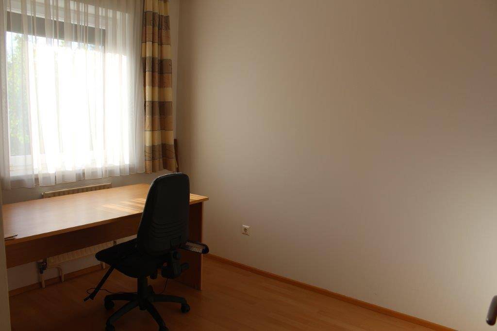 Arbeitszimmer mit Laminatboden, Schreibtisch, Bürostuhl und großem Fenster.