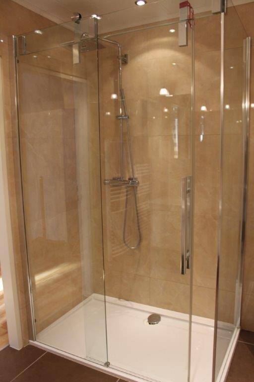 Moderne Duschkabine mit Glaswänden und beigefarbenen Fliesen im Badezimmer.