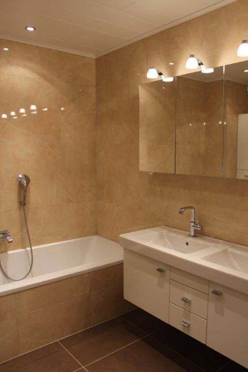 Modernes Badezimmer mit beigefarbenen Fliesen, Doppelwaschbecken und Badewanne.