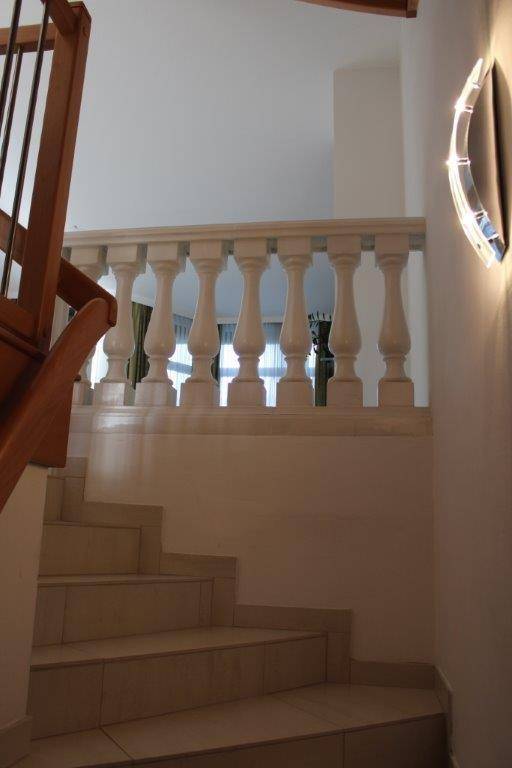Treppenaufgang mit weißen Balustraden und hellen Fliesenstufen, beleuchtet von einer Wandleuchte.