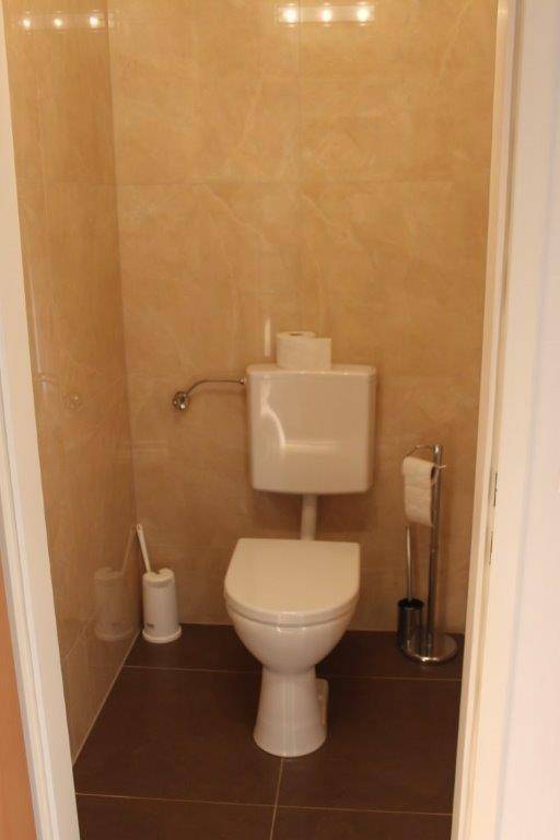 Separates WC mit beigefarbenen Wandfliesen und dunklem Boden in einem kleinen Raum.