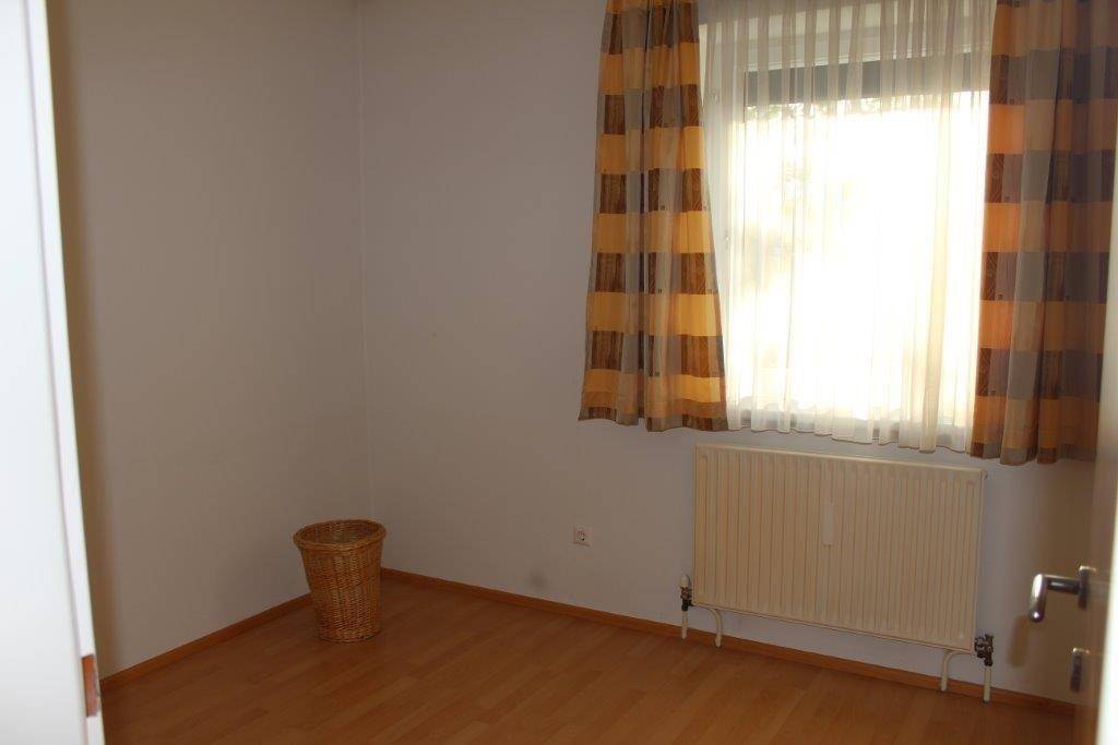 Leeres Zimmer mit Laminatboden, Fenster und einem Heizkörper, bereit zur Einrichtung.