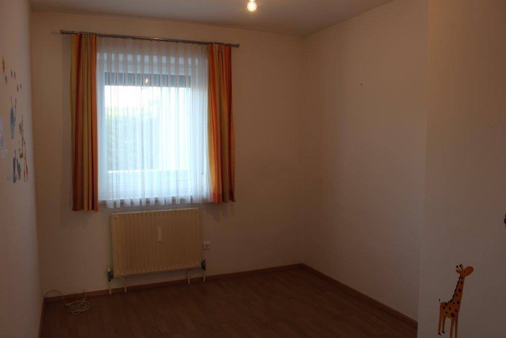 Helles Schlafzimmer mit Laminatboden, Fenster und einem Heizkörper unter dem Fenster.