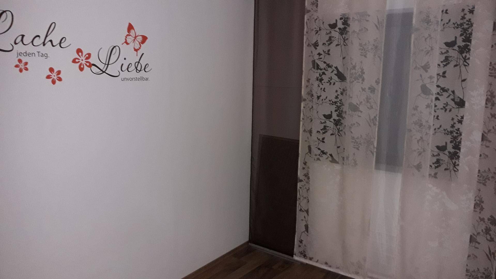 Innenraum mit weißer Wanddekoration, floralen Vorhängen und dunklem Schrank.