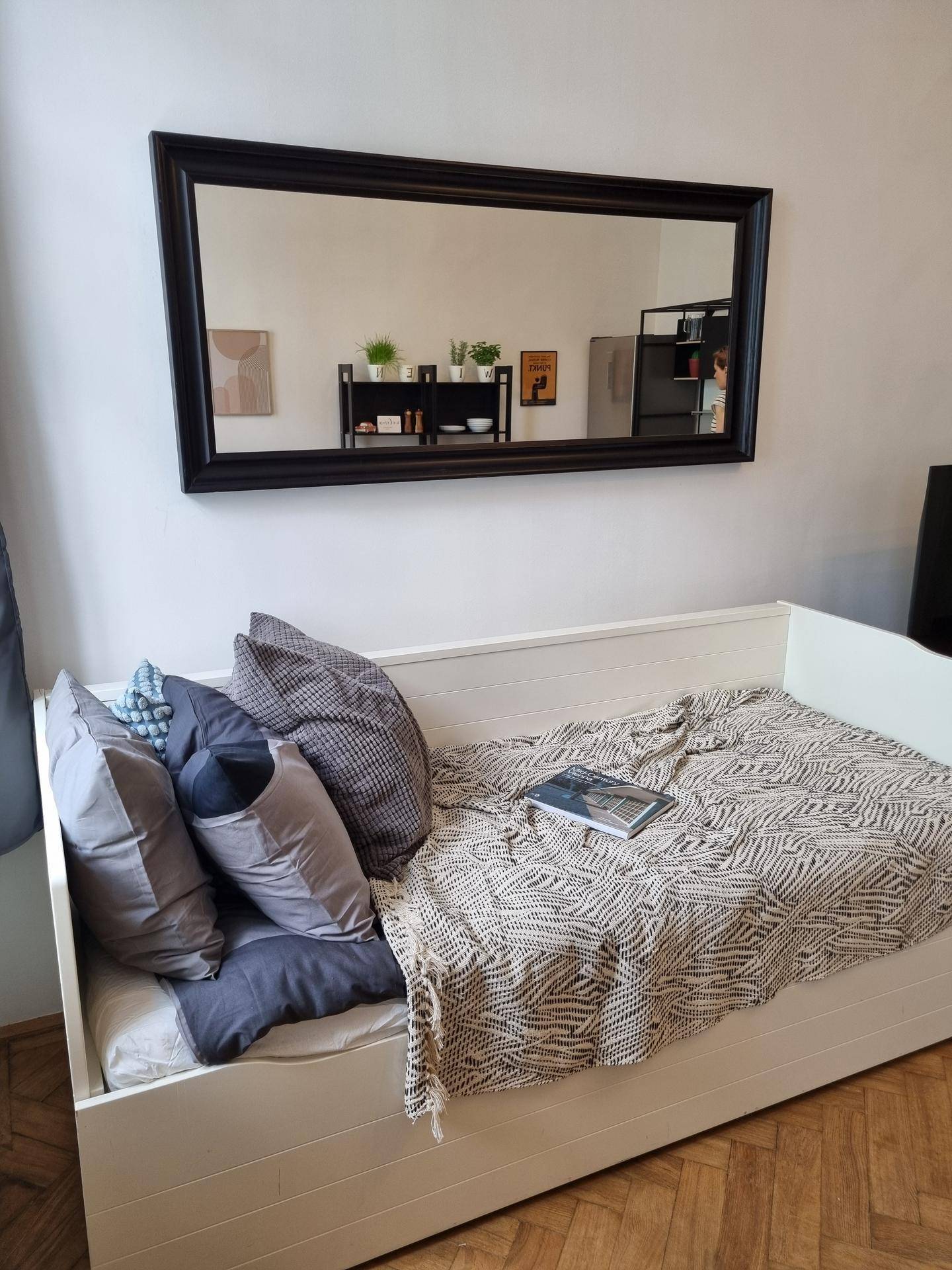 Gemütliches Tagesbett mit Kissen und Decke, darüber ein großer Spiegel im Schlafbereich.